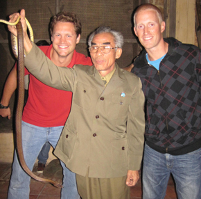 snakecharmer2 The owner took us across the street to a room with a thatch hut. The employees eagerly pulled out 4 snakes from a bag and handed over the knife to Eric. Eric sliced down the belly of the snake and the employee dripped the snake blood into a large glass. The heart was cut out of the snake next and placed into a shot glass. Snake hearts continue beating for 10 minutes after they are dead so this process had to be fairly quick because the tradition is to eat the heart while it still beats. The other two boys did two more killing and I watched as the employee did my snake (there was no way I could cut into a still squirming snake). The restaurant set up a table and passed out the shots that included snake blood, still beating snake heart and some rice wine.